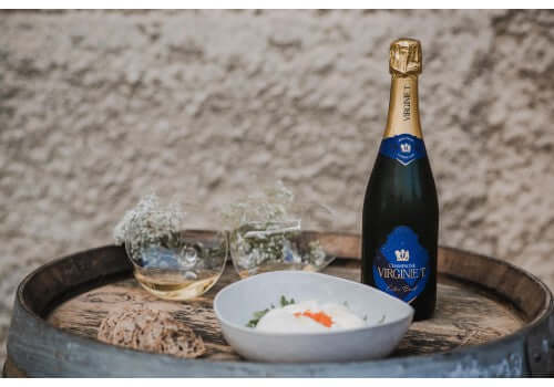 Champagne Virginie T Extra Brut NV bottle with a gourmet dish on a rustic wooden barrel.