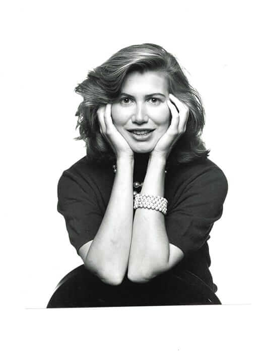 Black and white portrait of a woman with long hair, smiling and resting her chin on her hands.